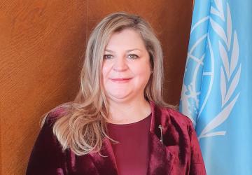 Official photo shows Catherine smiling to the camera, wearing a wine coloured jacket and blouse. She stands by the UN flag.