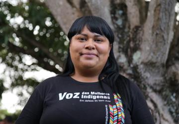 An indigenous woman smiles proudly wearing a t-shirt that reads Voice of the Indigenous women