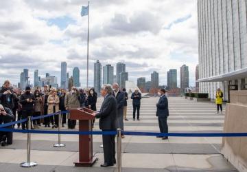 A man speaks to reporters outside a building on a grey windy day.