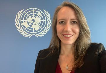 Woman wearing a black suit standing in front of a blue wall with the UN logo