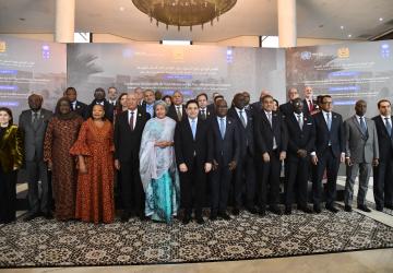 A group of people, men and women in suits and traditional formal clothing gathered in a hall