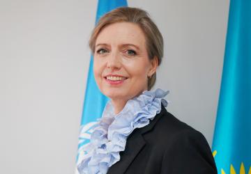 A headshot of a woman in a black suit blazer and blue scarf
