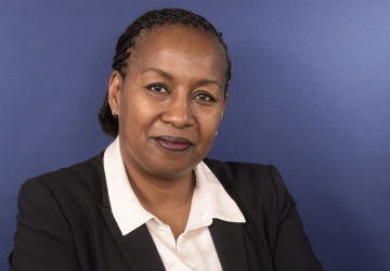 A headshot of a woman in a black suit and a white shirt against a blue background