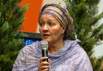 A woman in a purple dress speaks into a microphonne