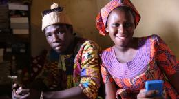 Dos jóvenes senegaleses, un hombre y una mujer, miran orgullosos a la cámara mientras sostienen sus teléfonos móviles.