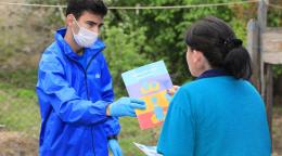 Une femme tend une brochure à un jeune homme portant des gants et un masque de protection.