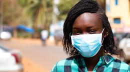 A mid-close up of an adolescent girl wearing a face mask poignantly looking at the camera. 