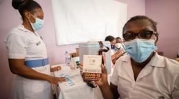 A healthcare professional at a vaccination site proudly holds up a COVID-19 vaccination card that verifies she received the vaccine.
