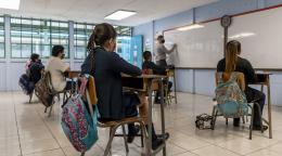 Children seated at desks attending in-person school at a social distance wearing masks. 
