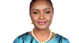 A woman with a light blue dress and her hair up in a bun smiles at the camera.