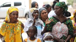 Un groupe de femmes portant chacune un couvre-chef et accompagnées d'une petite fille discute dans la rue.