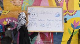 A woman points to a whiteboard with information on Covid-19 safety protocols. 