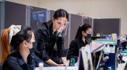 Women wearing protective masks and face shields work together at a desk at an office.