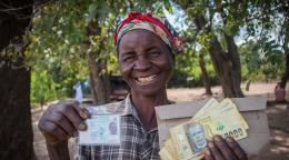 A smiling woman holds up cash assistance and her identification card. 