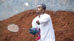 A young man with disabilities plays badminton outdoors. 
