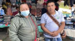 A woman wearing a facemask and a man are standing side by side at a street market. 