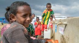 أطفال صغار يلعبون بالقرب من صنبور المياه في بيئة جافة.