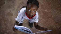 Niña mirando a la cámara con un libro abierto en sus manos.