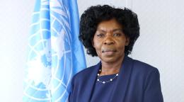 Una mujer con un traje azul oscuro se encuentra delante de una bandera de las Naciones Unidas.