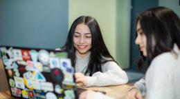 فتاتان تجلسان على مكتب وتعملان على جهاز حاسوب محمول.