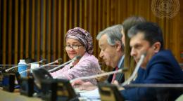 A woman in a light colored shawl and headwrap turns toward the camera while speaking on a panel. 