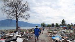 A man scours debris and building remnants on a waterfront.
