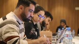 Two young men and a young woman are photographed in profile working side by side in a training room