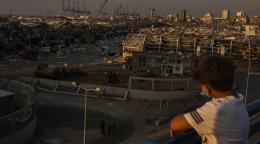 Un jeune garçon regarde le port dévasté de la ville de Beyrouth depuis un balcon.