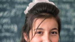 Un primer plano de una chica sonriendo a la cámara frente a una pizarra escrita.