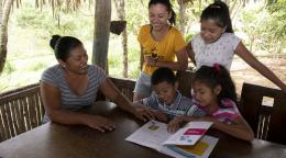 أربعة أطفال وامرأة يقرأون مواد تعليمية خلف طاولة خشبية.