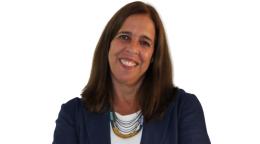 A woman in a blue blazer crosses her hands and smiles for the camera.