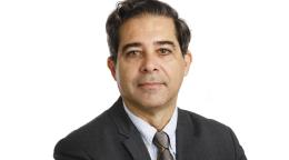 Un hombre con corbata y traje, funcionario de las Naciones Unidas, sonríe para la cámara.