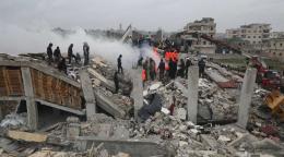 Several people standing on debris from building destroyed by earthquake in Syria