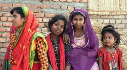A group of girls in colorful outfits from Nepal huddle together and smile. 