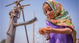 Young girl catching water from a pipe in Pakistan