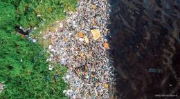 A large track of plastic waste between green land on one side and water on the other side