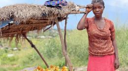 A girl in a pink dress stands by a straw hut