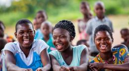 three young people sit next to each other outside laughing towards camera