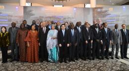 A group of people, men and women in suits and traditional formal clothing gathered in a hall