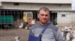 Мужчина с повязкой поддерживающей для руки стоит на фоне фермы