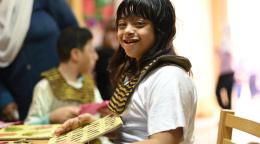 A picture of a girl in a white shirt, playing with a wooden card in a school classroom