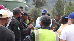 A group of people gather and talk; each person dressed in dark clothes and caps, with one person in the middle in a neon coloured jacket.