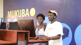 A man and a woman wearing white stand at a desk with a computer in front of them