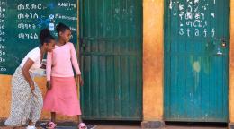 Two girls in front of a school classroom; one of the girls is on a skateboard