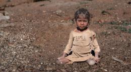 一个小女孩穿着破烂的衣服坐在一片贫瘠的土地上。