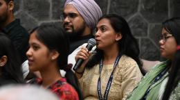 A young woman is holding a microphone and speaking to an audience