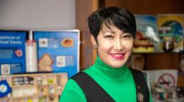 A woman wearing a green top and a blazer looks at the camera and smiles