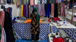 A woman in a dark green dress stands in front of rolls of cloth in a small shop