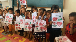 A group of children in school holding up their worksheet and making peace signs with their hands