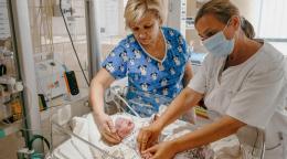 Two nurses care for a newborn child in a medical unit, connected to wires.